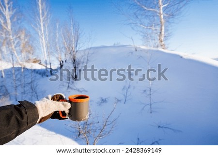Man holding a mug of tea in his hand on the background of a snowy mountain in the forest, drinking tea in winter in nature, a glass made of aluminum with a silicone border. High quality photo