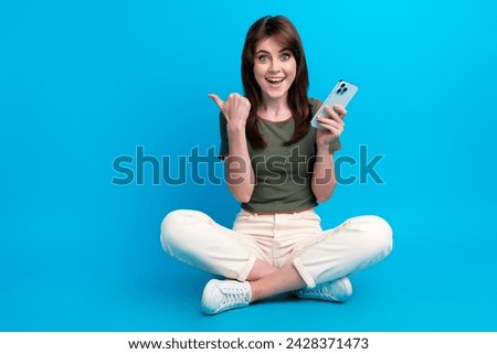 Full size photo of impressed woman wear green t-shirt sit hold smartphone indicating at sale empty space isolated on blue color background