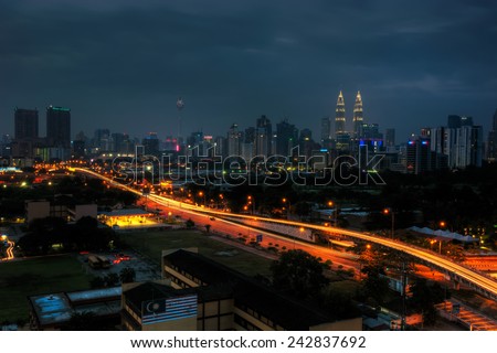 Long Exposure of Kuala Lumpur city at night with light trail along the highway roads moving and back from the city. Visible noise due to low light, soft focus, shallow DOF, slight motion blur. 
