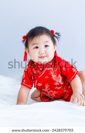 Chinese New Year concept, cute happy little girl in Chinese dress sitting in white living room. Cute Asian baby sitting in white living room, Chinese New Year concept