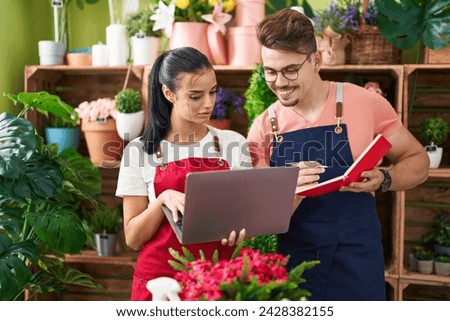 Man and woman florists using laptop writing on notebook at flower shop