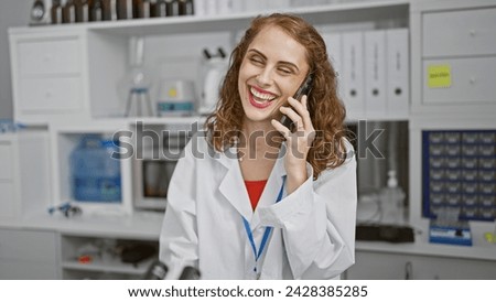 Smiling young woman scientist enthralled in marshaling medical marvels, animatedly talking on smartphone at her lab's work table