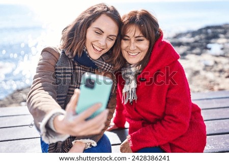 Two women mother and daughter make selfie by smartphone sitting on bench at seaside