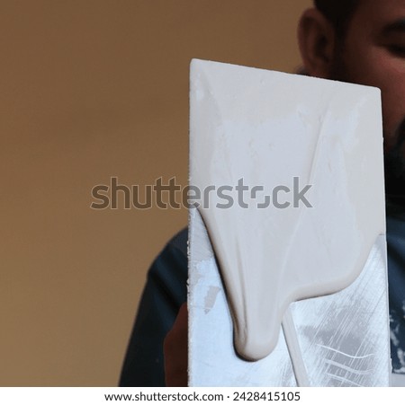 paint knife. Paint trowel in hand. application Paint paste white on wall internal. changing paint in the house  Royalty-Free Stock Photo #2428415105