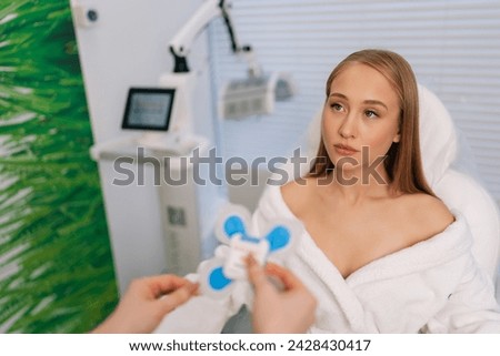 View from shoulder of unrecognizable female cardiologist puts holter sensors on woman patient with heart disease. Young woman during functional rehabilitation in cardiology room in clinic.