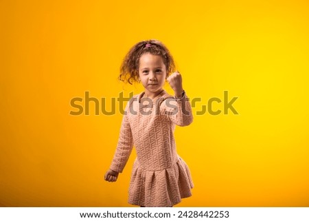 Portrait of enraged Child girl showing fist at camera on yellow background. Negative emotions concept Royalty-Free Stock Photo #2428442253