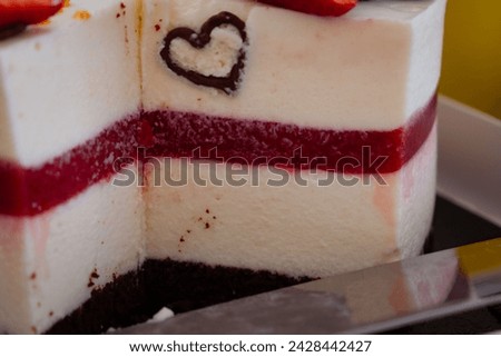 Close-up of a layered cake with vibrant red berry compote, chocolate heart decoration, and chocolate base, showcasing its texture and colors, ideal for sweet culinary themes.
