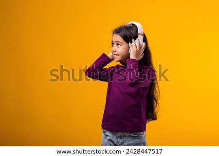 Portrait of smiling kid girl wearing pink dress enjoying music in headphones on yellow background. Lifestyle and leasure concept