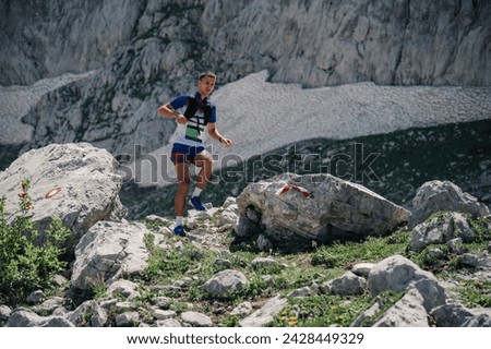 A skyrunner is running on rocky mountain. An extreme sportsman is practicing for ultramarathon in wild nature in mountains. A fit man is exercising and practicing in wilderness. Copy space. Royalty-Free Stock Photo #2428449329