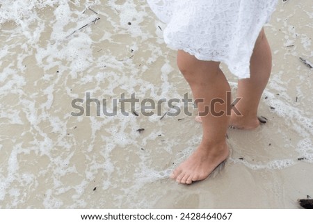 Half body of an unidentified person wet their feet in the beach sand. Relaxation concept. Royalty-Free Stock Photo #2428464067
