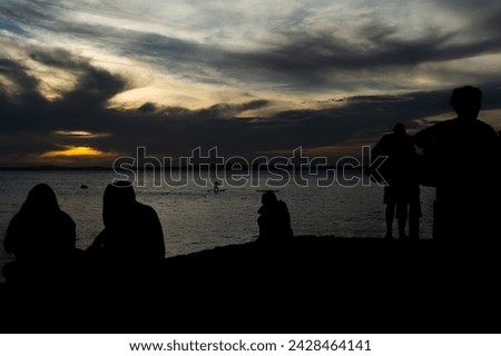 Silhouette of unidentified people enjoying dramatic sunset with dark clouds and sun in yellow color. City of Salvador, Bahia. Royalty-Free Stock Photo #2428464141