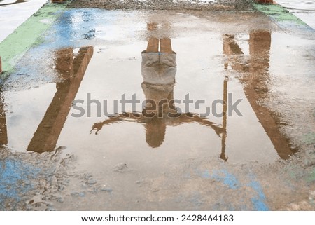 Reflection of an unidentified person in the puddle of water on the cement floor. Abstract photo, background and texture. Royalty-Free Stock Photo #2428464183