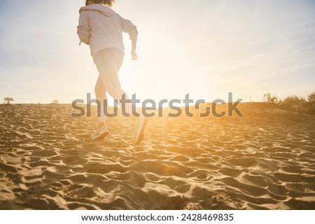 Rear view of sportswoman running on the sandy beach, burning calories. Photo with bokeh, sunbeams at sunset. People, active and healthy lifestyle, endurance, bodyweight training outdoor. Copy ad space