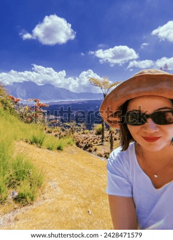 Pretty Asian girl wearing hat and sun glasses smiling as she is taking selphie picture against mountain scenery. Travel to hightkands. Soft focus. film grain pixel texture. Defocused.