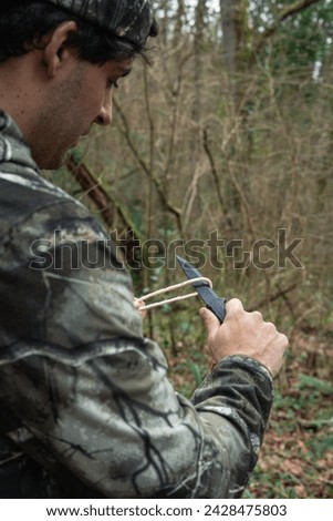 closeup from behind In this striking image, an intrepid explorer is immersed in the heart of the forest, facing challenges with skill and bravery. Armed with his survival knife, he cuts a rope  Royalty-Free Stock Photo #2428475803