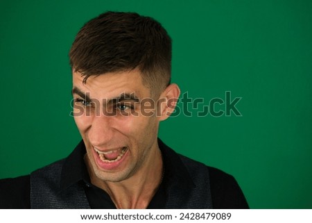 emotions of a handsome man guy on a green background chromakey close-up dark hair young man. Evil laughing of a man