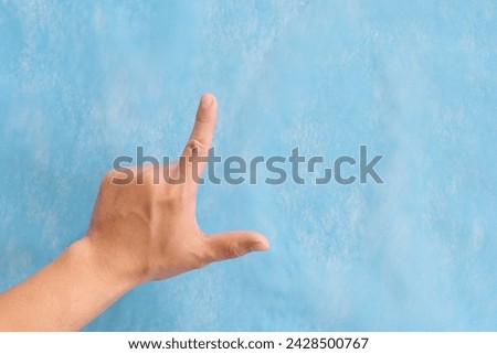 Young male Asian hand making loser sign or letter L isolated on blue background.