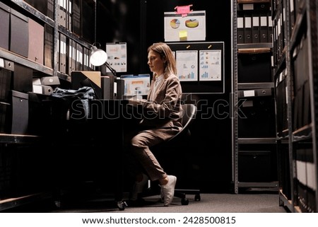 Businesswoman reading bureaucracy report, organizing corporate papers in storage room. Caucasian bookkeeper checking administrative documents, working overtime at office depository Royalty-Free Stock Photo #2428500815