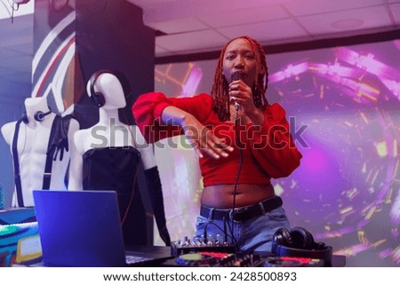 African american singer performing on stage at nightclub party. Woman dj singing in microphone and mixing tracks with electronic music digital station at club discotheque Royalty-Free Stock Photo #2428500893