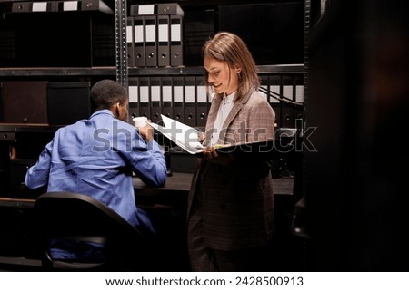 Workers discussing management report, analyzing administrative documents in corporate depository. Diverse employees reading bureaucracy record, discovering accountancy files in storage room Royalty-Free Stock Photo #2428500913