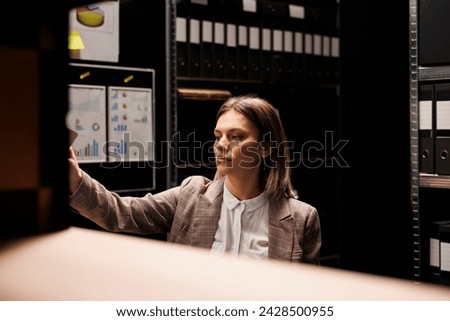 Manager working with bureaucracy files, analyzing bookkeeping record searching for management report. Bookepper standing overhours in arhive room, organizing depository documents Royalty-Free Stock Photo #2428500955