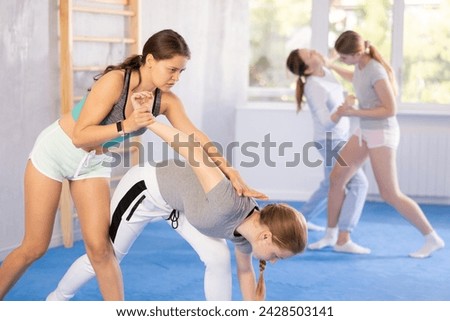 Determined adolescent girl attending self-defense classes at training center, applying armlock technique to female opponent in simulated sparring ..