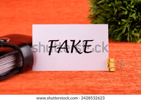 FAKE word written on a white card near the business card holder in black on an orange background