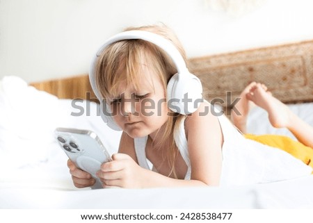 girl plays with smartphone and listens to music on headphones, watches cartoons on phone, online learning, online games