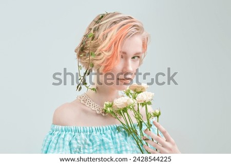 Beauty portrait. A tender blonde girl with a short haircut poses with cream rose flowers on a white studio background. Delicate feminine spring-summer look.