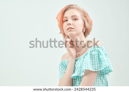 A cute blonde teenage girl with a short haircut in a summer sundress poses against a white wall. Delicate spring-summer look. Beauty, cosmetics. Copy space.