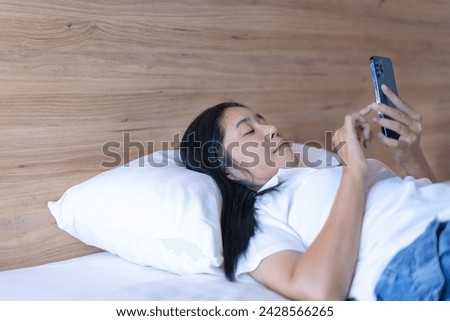 happy woman lying down and using the phone on a comfortable bed in the bedroom. View application Read news online Enjoy shopping on the internet. Mobile communication Weekend relaxation.