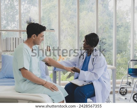Portrait patient caucasian man with woman nurse carer physical therapist African-American two people sitting talk helping support give advice and holding hand arm inside hospital indoor room service.