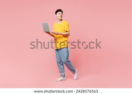 Full body side view young IT man he wears yellow t-shirt casual clothes hold use work on laptop pc computer look aside on area isolated on plain pastel light pink background studio. Lifestyle concept