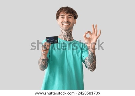 Tattooed young man with credit card showing OK on light background