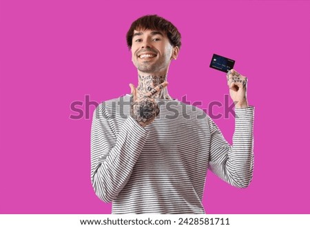 Tattooed young man pointing at credit card on purple background