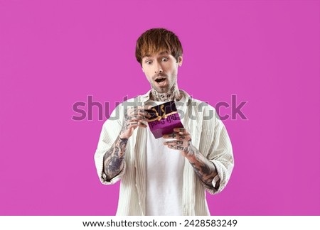 Surprised young tattooed man with gift card on purple background