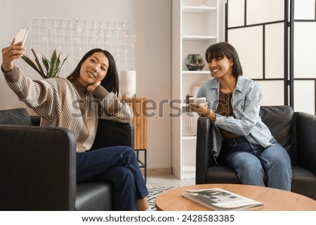 Young women in black armchairs taking selfie at home