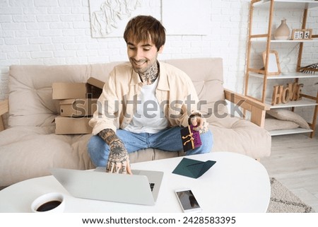 Young tattooed man with gift card and laptop shopping online at home