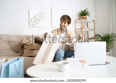 Young tattooed man with shopping bag and gift card on table at home