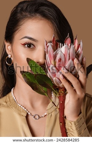 Young Asian woman with beautiful protea flower on brown background, closeup