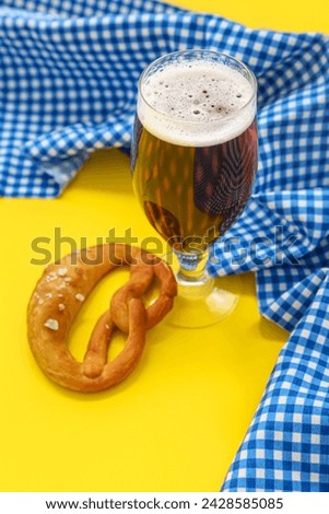 Soft pretzel and glass of beer on yellow background