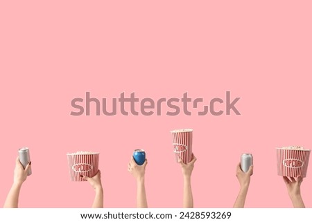 Hands holding buckets with popcorn and drinks on pink background