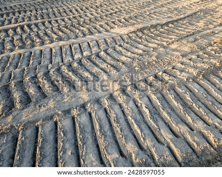 Caterpillar or tank tread trails imprinted by bulldozers or heavy equipment with continuous track in ground on excavation site. Pattern marks in textured brown earth. Royalty-Free Stock Photo #2428597055