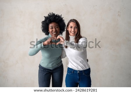 Young women of different ethnicity making a heart shaped gesture against a studio background.