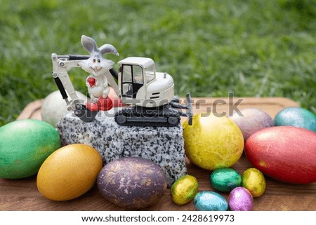 model of a toy excavator on a piece of granite, a souvenir rabbit, colorful eggs. Easter spring holiday concept for congratulations from construction companies