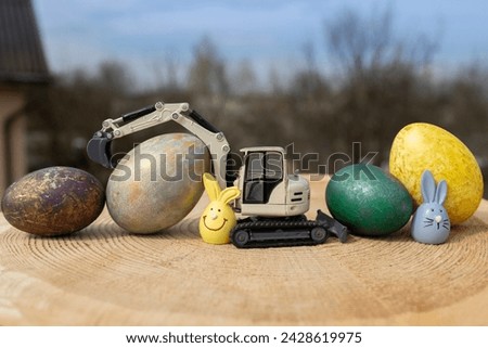model of a toy gray excavator and multi-colored Easter eggs on a wooden stump. Easter spring holiday concept. greeting card from construction companies