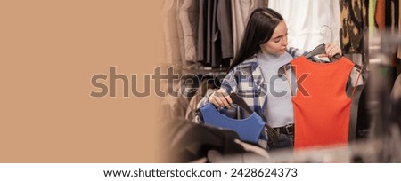 Shopping concept. Beautiful woman choosing dress during shopping at garments apparel clothing shop. Girl trying dress near mirror on room. Banner. Copy space
