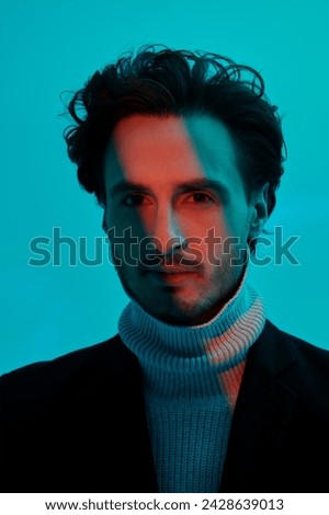 Portrait of a handsome brunette man with curly hair posing in blue lighting with a red stripe light. Color, fashion and style. Art Fashion photo.