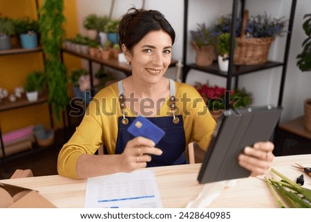 Middle age hispanic woman florist using touchpad and credit card at flower shop