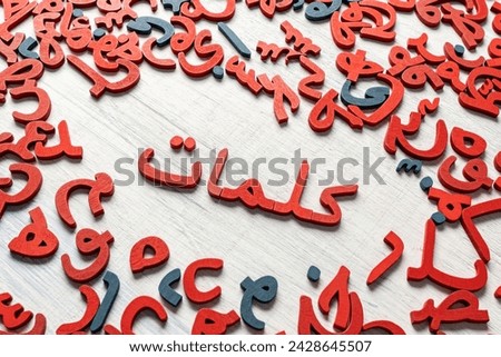 Topview picture of a group of Arabic letters made of wood,  translation: the word ( words) in the middle, 